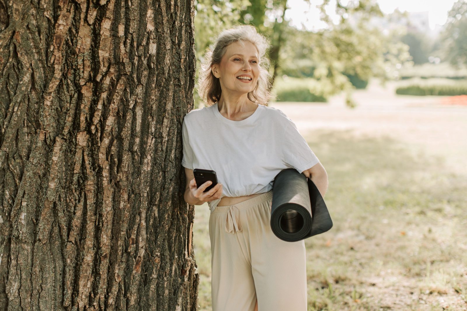 A woman in midlife carrying an exercise mat outdoors in a park